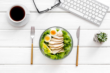 Healthy dinner in bowl near keyboard and tea on white wooden background top view