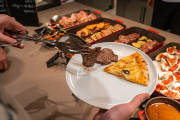 Human hand using tongs picking beef steak into his plate