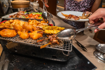 Human hand picking grilled chicken skewers in barbecue buffet