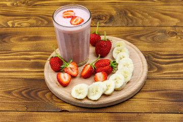 Glass of fresh smoothie of strawberry and banana on a wooden table