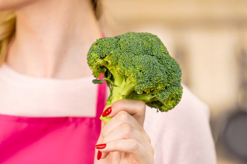 Woman in kitchen holding green fresh broccoli. Housewife cooking. Healthy eating, vegetarian food, dieting and people concept.