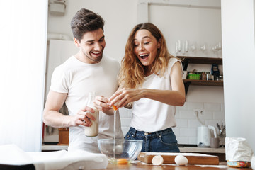 Image of cheerful young couple cooking breakfast together in apartment