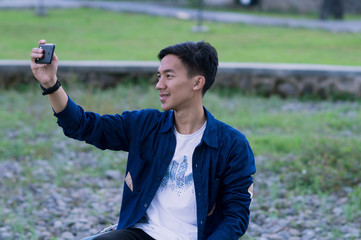 Happy young Asian men make selfies on smartphones with a garden background - photo