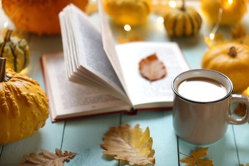 Autumn books. Tea mug, open book, set of pumpkins with a shining garland on a blue wooden...