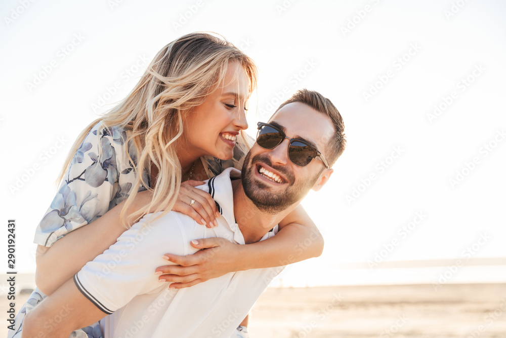 Sticker photo of unshaven happy man smiling and giving piggyback ride seductive woman while walking on sunny