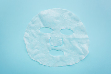 Sheet facial mask on pastel blue paper background. Skin care, dermatology, beauty concept. Top view, flat lay, mockup, overhead, copy space, template