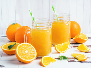 Orange juice in glass jars and fresh oranges on a white wooden rustic background.