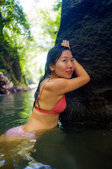 young beautiful happy Asian Chinese woman in bikini enjoying holidays at tropical forest refreshing relaxed in natural pool delighted by the tranquility at jungle lake