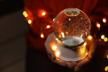 Woman holding snow globe and Christmas lights in darkness, closeup