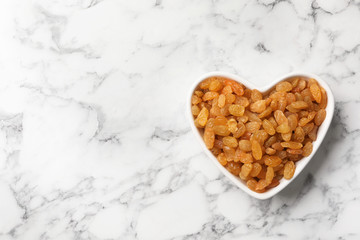 Heart shaped plate with raisins and space for text on marble background, top view. Dried fruit as...