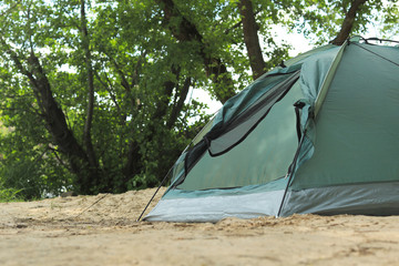 Modern camping tent near trees in wilderness