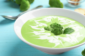 Bowl of cheese cream soup with broccoli served on blue wooden table, closeup