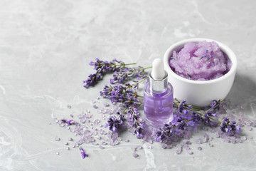 Natural cosmetic oil, bath salt, scrub and lavender flowers on grey marble table, space for text