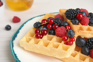 Delicious waffles with fresh berries served on white wooden table, closeup