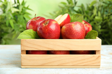 Wooden crate with ripe juicy red apples on white table against blurred background