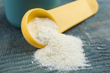 Overturned measuring scoop with protein powder on blue wooden table, closeup