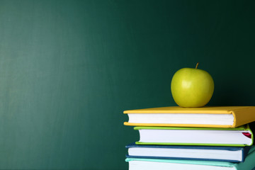 Books and apple near green chalkboard, space for text. School education
