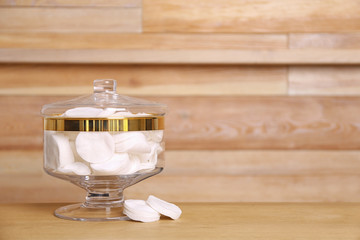 Composition of glass jar with cotton pads on table near wooden wall. Space for text