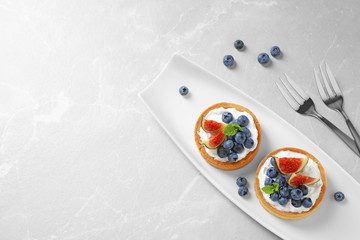 Tarts with blueberries and figs on marble table, flat lay with space for text. Delicious pastries