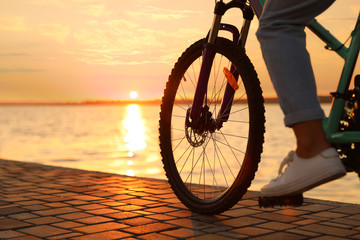 Fototapeta na wymiar Woman riding bicycle on embankment at sunset, closeup