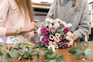 Close-up flowers in hand. Florist workplace. Woman arranging a bouquet with roses, carnation and...