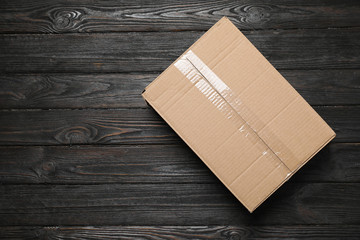 Closed cardboard box on black wooden background, top view. Space for text