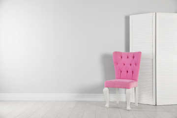 Stylish pink chair and folding screen near white wall. Space for text