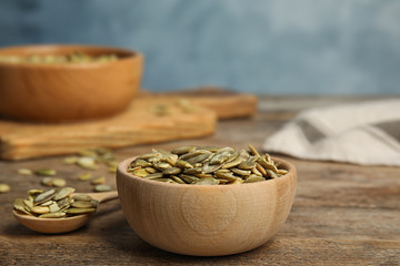 Bowl and spoon of raw peeled pumpkin seeds on wooden table. Space for text