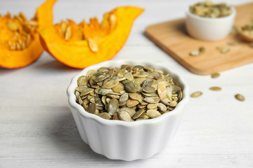 Bowl of raw pumpkin seeds on white wooden table