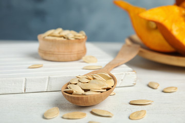 Spoon of raw pumpkin seeds on white wooden table