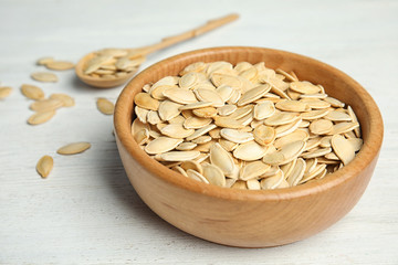 Bowl of raw pumpkin seeds on white wooden table