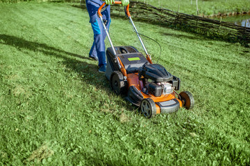 Gardener cutting grass with gasoline lawn mower on the backyard, close-up view