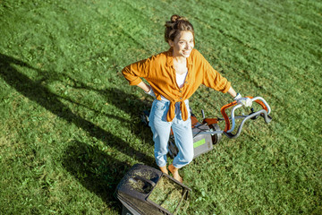 Portrait of a beautiful young woman dressed casually resting while cutting grass with lawn mower on...