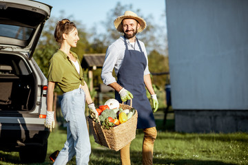 Man and woman carrying basket full of freshly picked up homegrown vegetables near the car at the...