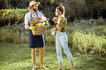 Man and woman carrying basket full of freshly picked up homegrown vegetables at the countryside on...