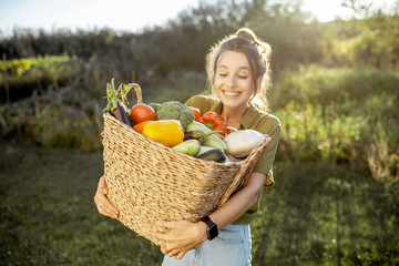 Portrait of a beautiful young woman with basket full of freshly picked up vegetables standing in...