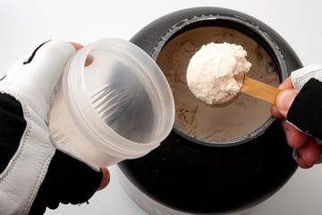 Weight training, wellness and exercising conceptual idea with masculine hands, wearing protection gloves for the gym, preparing a protein shake by filling the shaker with muscle gain powder isolate