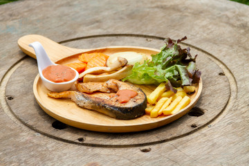One piece of baked salmon grilled pepper lemon and salt on a wooden plate