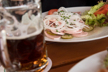 Mann mit dunklen Bier und Bayrischen Wurstsalat aus Stadtwurst, Zwiebel Ringe, saure Gurken und Schnittlauch im Biergarten