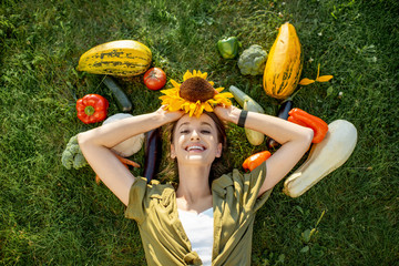 Young smiling woman lying on the grass surrounded by freshly picked up homegrown vegetables....