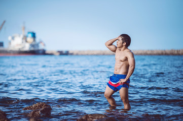 Bodybuilders are posing to show strength at the rocks by the sea.