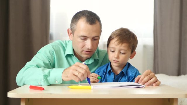 Happy family: dad and son spend time together. Father and son draw colored felt pen. Lifestyle, relationships, children's interests.
