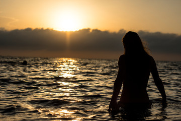 silhouette of young woman in the water at sunset
