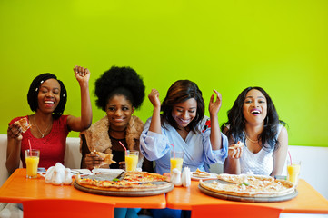 Four young african girls in bright colored restaurant eating pizza and having fun together.