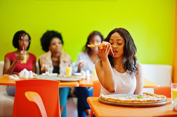 African woman with pizza sitting at restaurant against dark skinned girls.