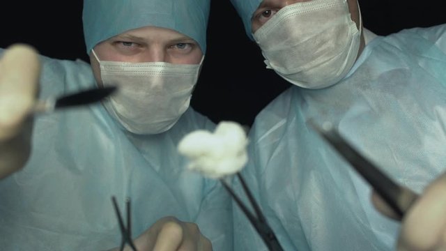 Surgeons lean towards the patient before surgery, first person view. Doctors with scalpel, grasper or forcep are ready to start cut a patient's tissues in hospital.