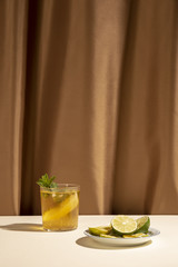 Delicious cocktail drink with mint leaves and lime slices on table in front of brown curtain