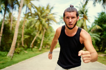 Healthy lifestyle. Jogging outdoors. Young strong man is running under palm trees.