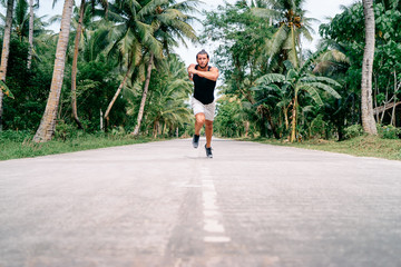 Healthy lifestyle. Jogging outdoors. Young strong man is running under palm trees.