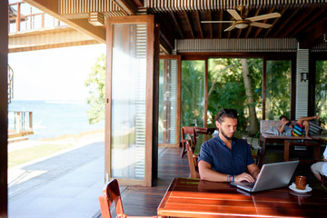 Freelance concept. Young  bearded man working on laptop computer while sitting on cafe terrace.
